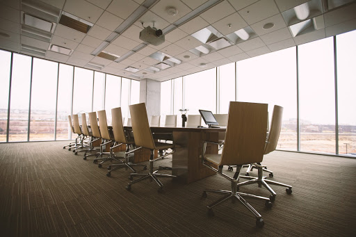 A number of rolling chairs line a long table in an empty meeting room with floor to ceiling windows. 