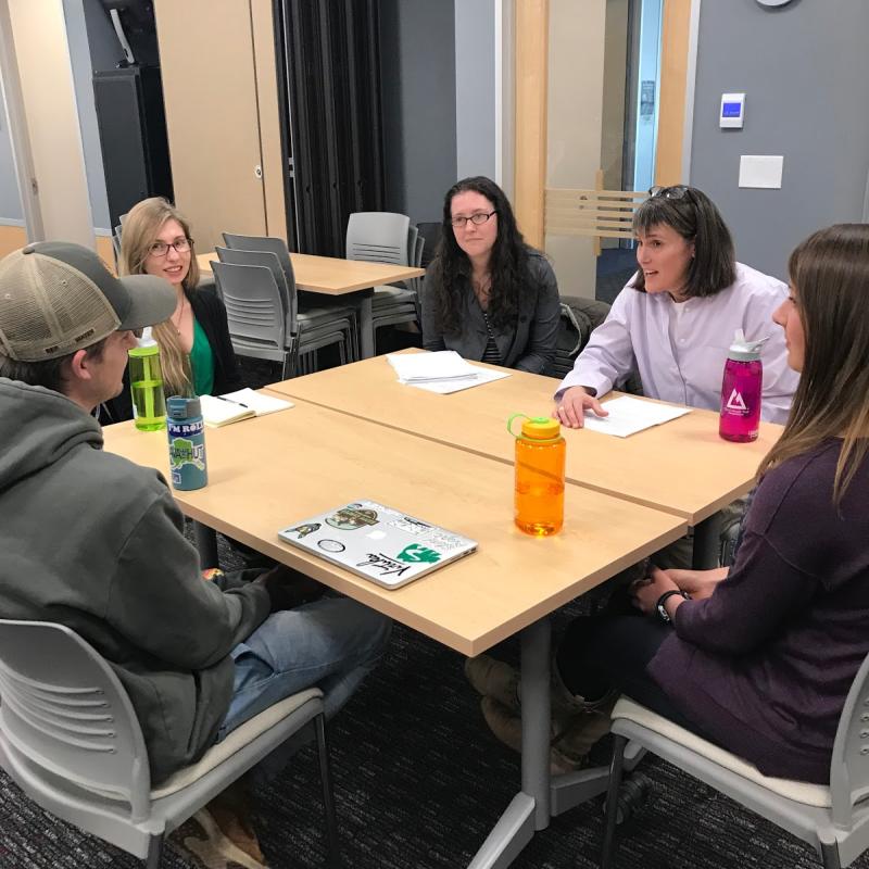 Students gathered around a large square table, listening to USGS’ Vivian Hutchison